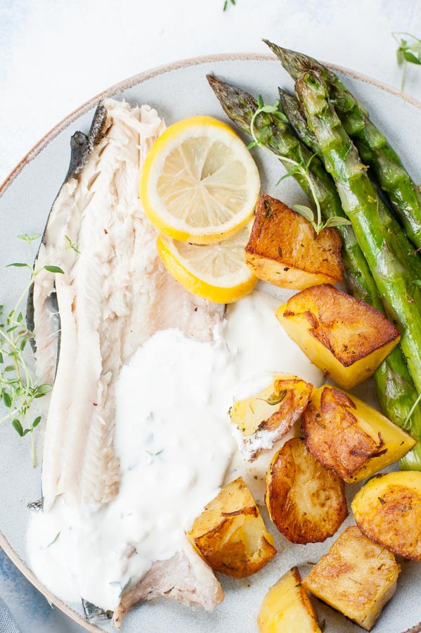 Close up shot on whole roasted trout with potatoes, asparagus and thyme-garlic dip.