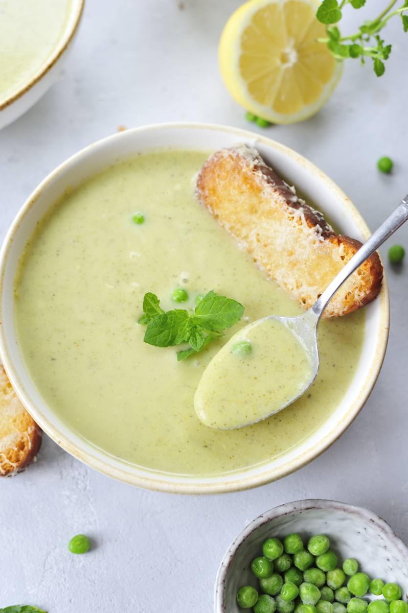 Creamy zucchini soup in a white bowl garnished with mint leaves and cheese toast on the side.