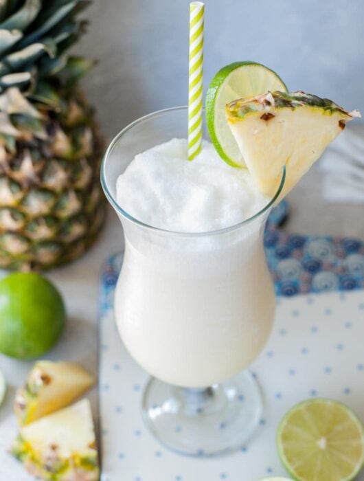 One glass with pina colada drink garnished with pineapple wedge and lime slice.