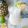 One glass with pina colada drink garnished with pineapple wedge and lime slice.