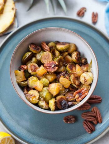 Roasted brussel sprouts with pineapple and pecans in a grey bowl.