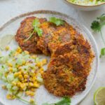 Sweet potato zucchini fritters with corn cucumber salsa on a white plate.
