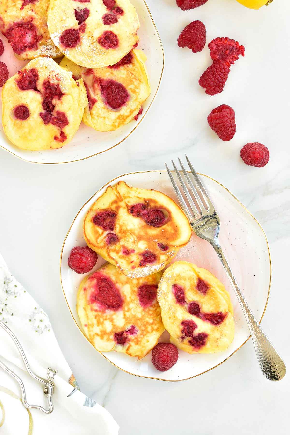 Lemon ricotta pancakes with raspberries on a rose plate.