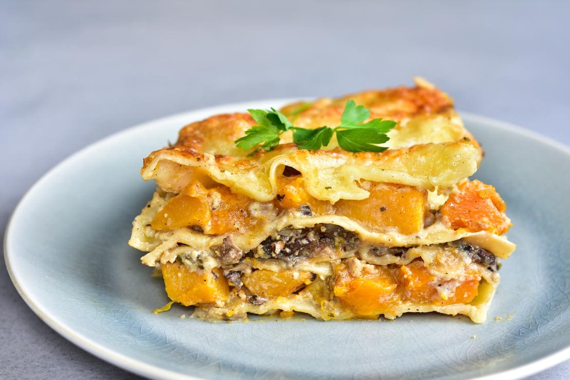 A piece of white lasagna with pumpkin and mushrooms on a green plate.