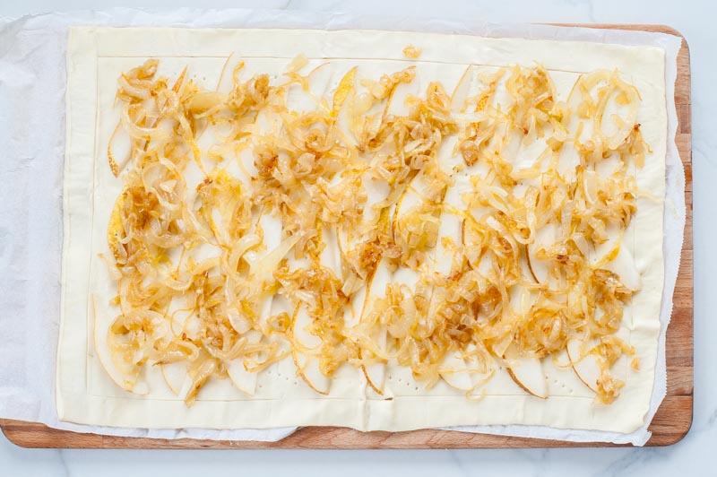 raw puff pastry topped with caramelized onions and pear slices 