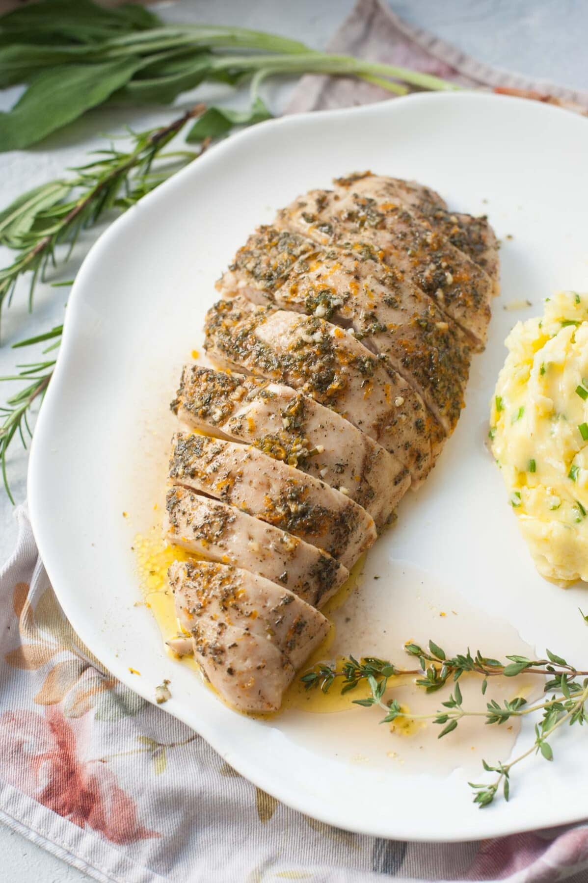 Baked turkey tenderloin cut into slices on a white plate. Herbs in the background.