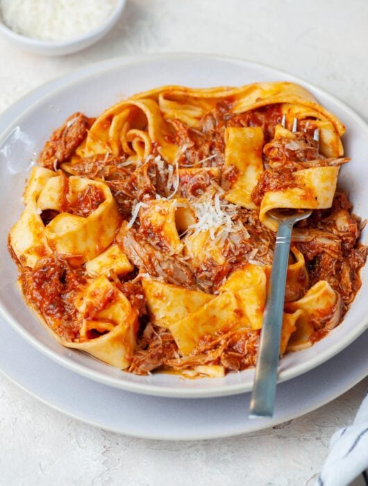 Duck ragu with pappardele pasta in a beige plate.