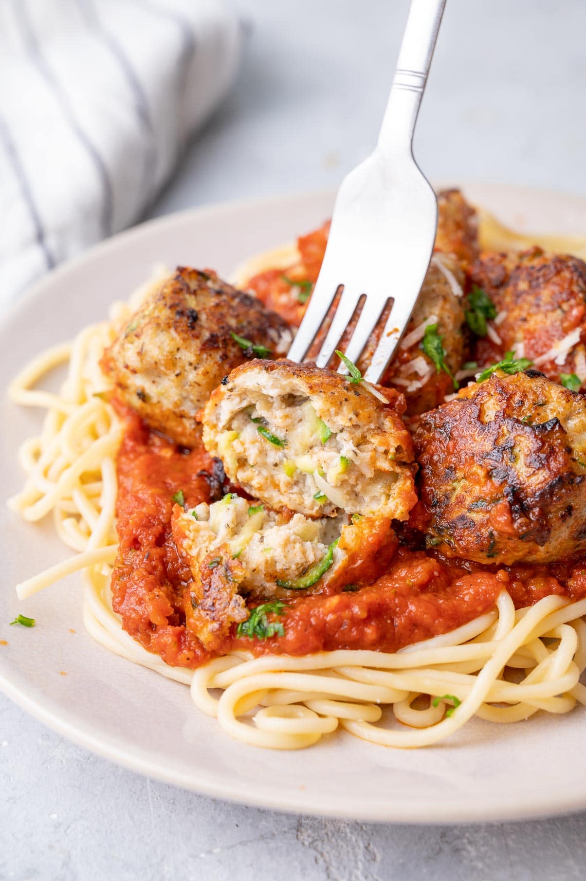 Turkey zucchini meatballs served with tomato sauce and spaghetti on a beige plate. One meatball is cut in half.