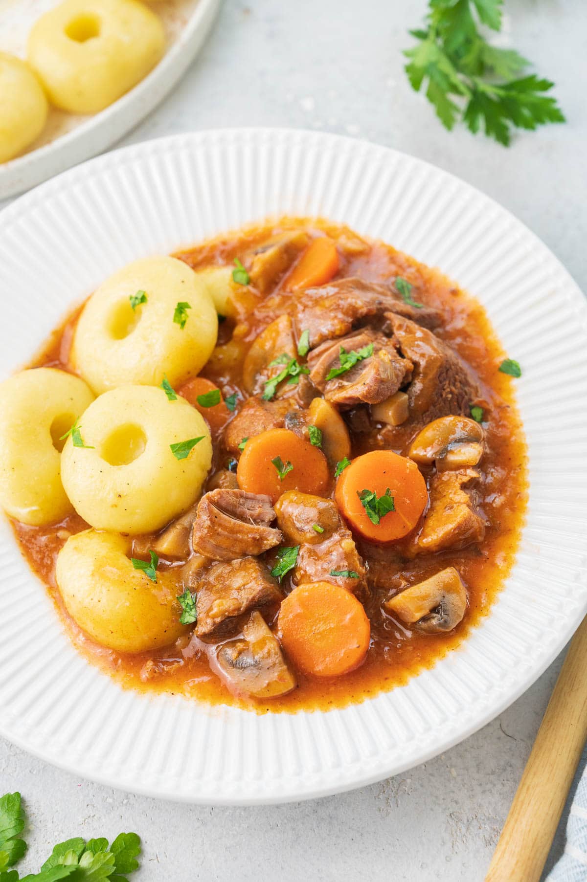 Polish pork stew served with dumplings in a white plate.