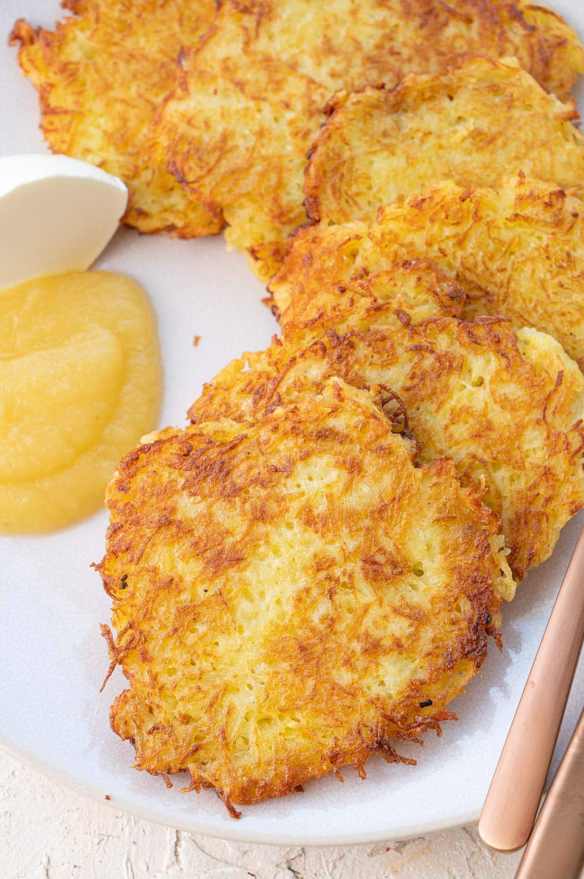 German potato pancakes served with sour cream and apple sauce on a beige plate.