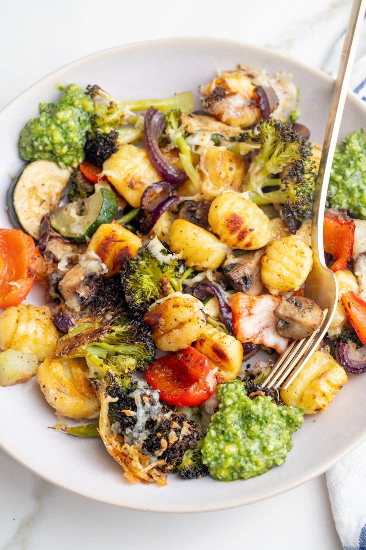 Baked gnocchi with vegetables and basil pesto on a beige plate.