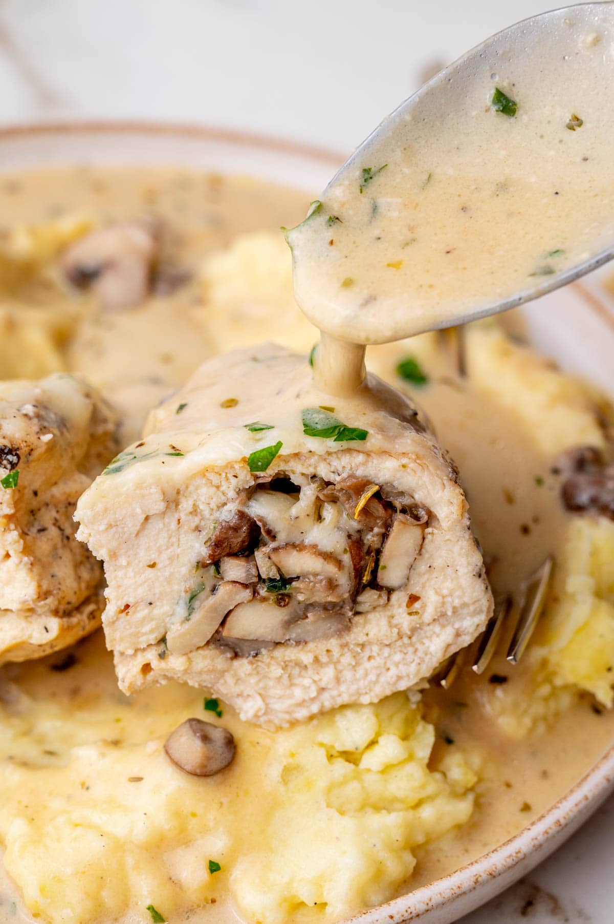 Cut in half mushroom-stuffed chicken breast is being poured with creamy sauce.