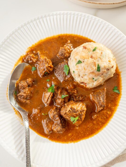 Viennese goulash served with Semmelknödel in a white plate.