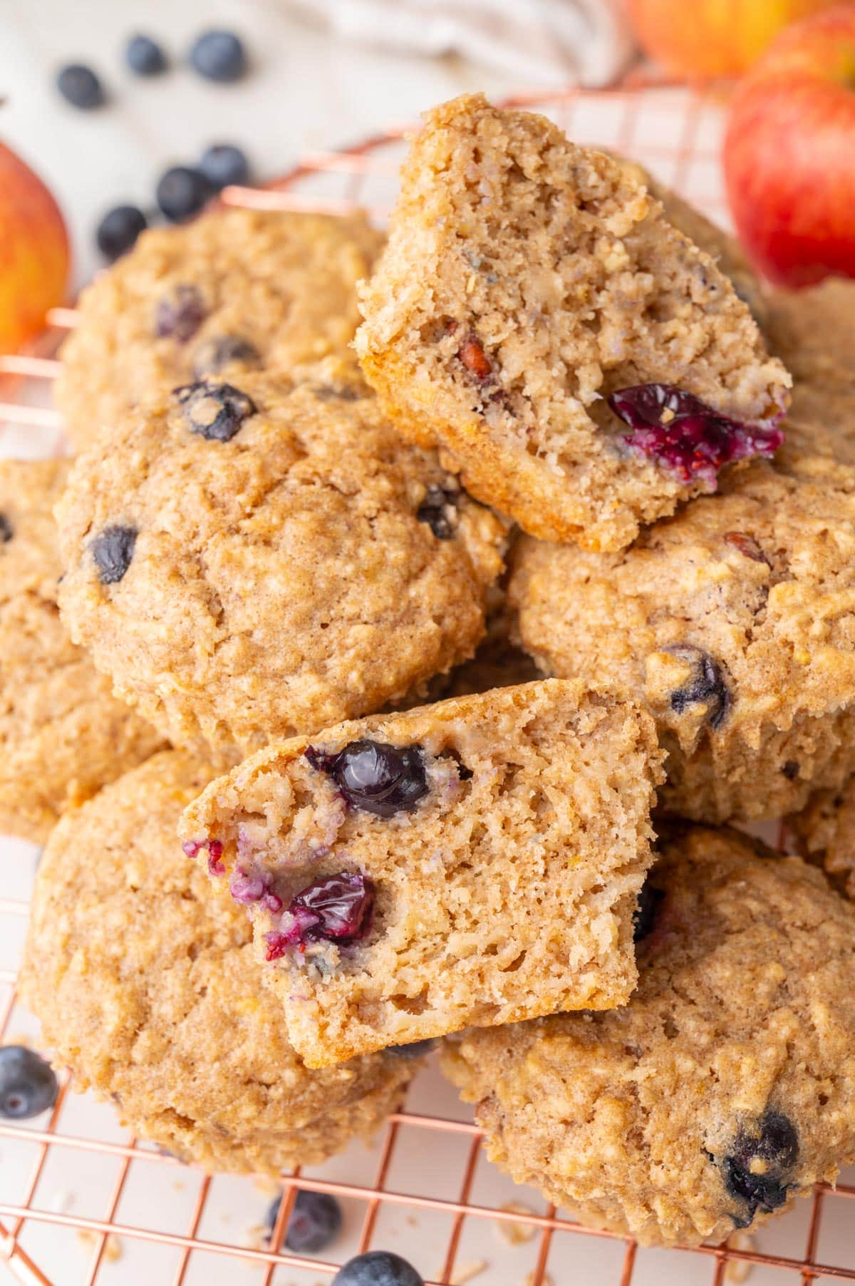 Freshly baked healthy breakfast muffins stacked on a wire cooling rack, with one muffin cut in half to show its soft and moist texture with visible blueberries inside.