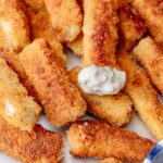 Close-up of crunchy homemade fish sticks topped with creamy tartar sauce.