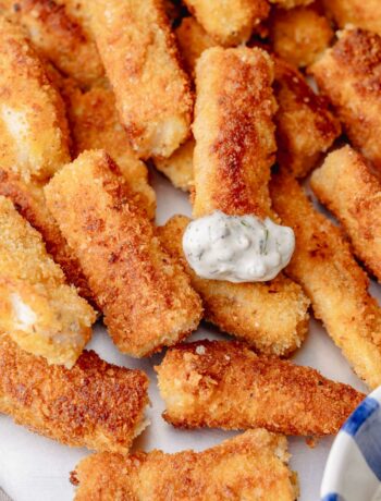 Close-up of crunchy homemade fish sticks topped with creamy tartar sauce.