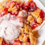 Close-up of a serving of strawberry rhubarb crumble on a plate with melted ice cream and a spoon.