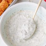 Close-up of a creamy homemade tartar sauce in a white bowl, with a spoonful lifted above the sauce.