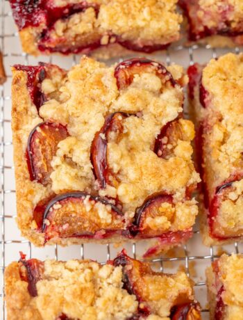 Close-up of a slice of German plum cake with a buttery crumb topping and baked plum halves, showing crisp edges and juicy fruit.