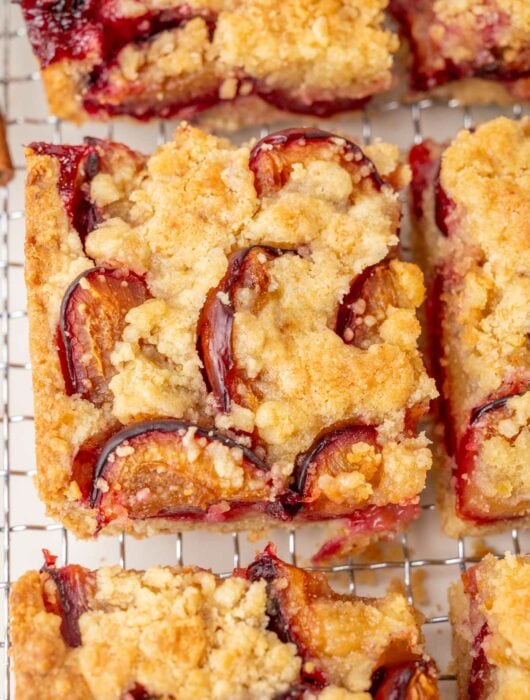 Close-up of a slice of German plum cake with a buttery crumb topping and baked plum halves, showing crisp edges and juicy fruit.