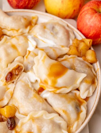 Apple pierogi on a beige plate served with caramel sauce and sour cream.