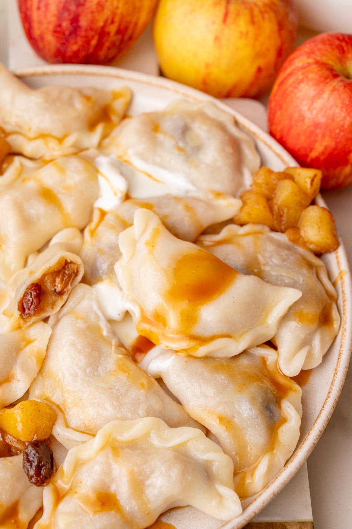 Apple pierogi on a beige plate served with caramel sauce and sour cream.