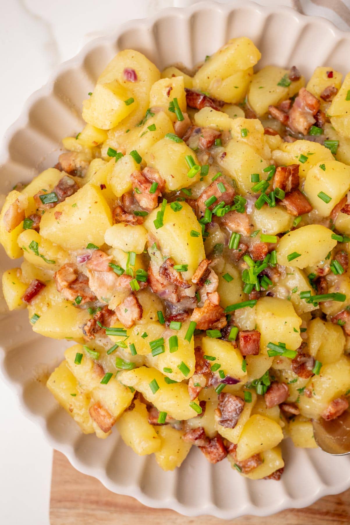 German potato salad with bacon and chives in a beige bowl.