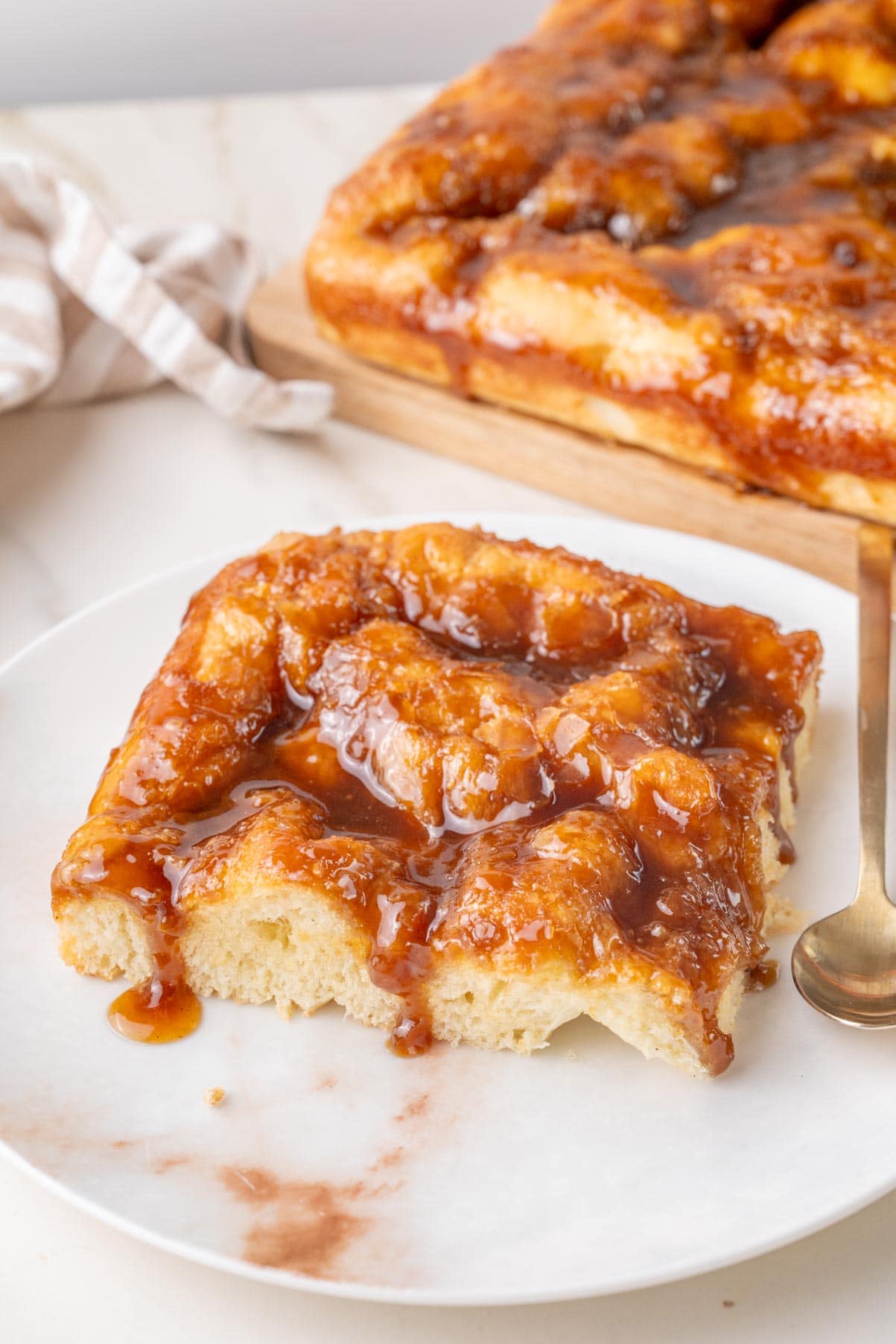 A piece of Brunsviger cake on a white plate with the whole cake in the background.