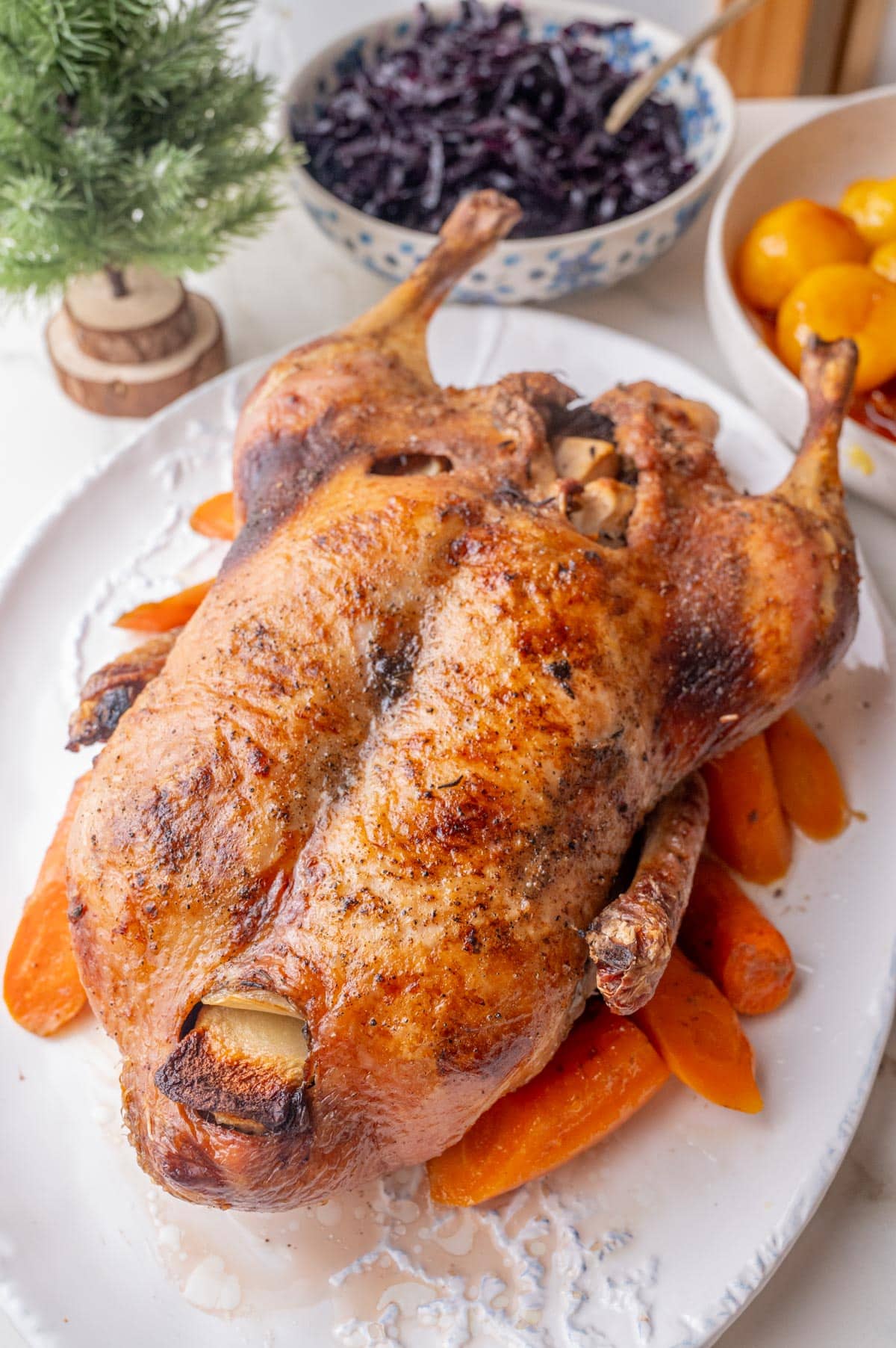 Danish Christmas Duck on a white plate. Red cabbage, caramel potatoes, and Christmas decoration in the background.
